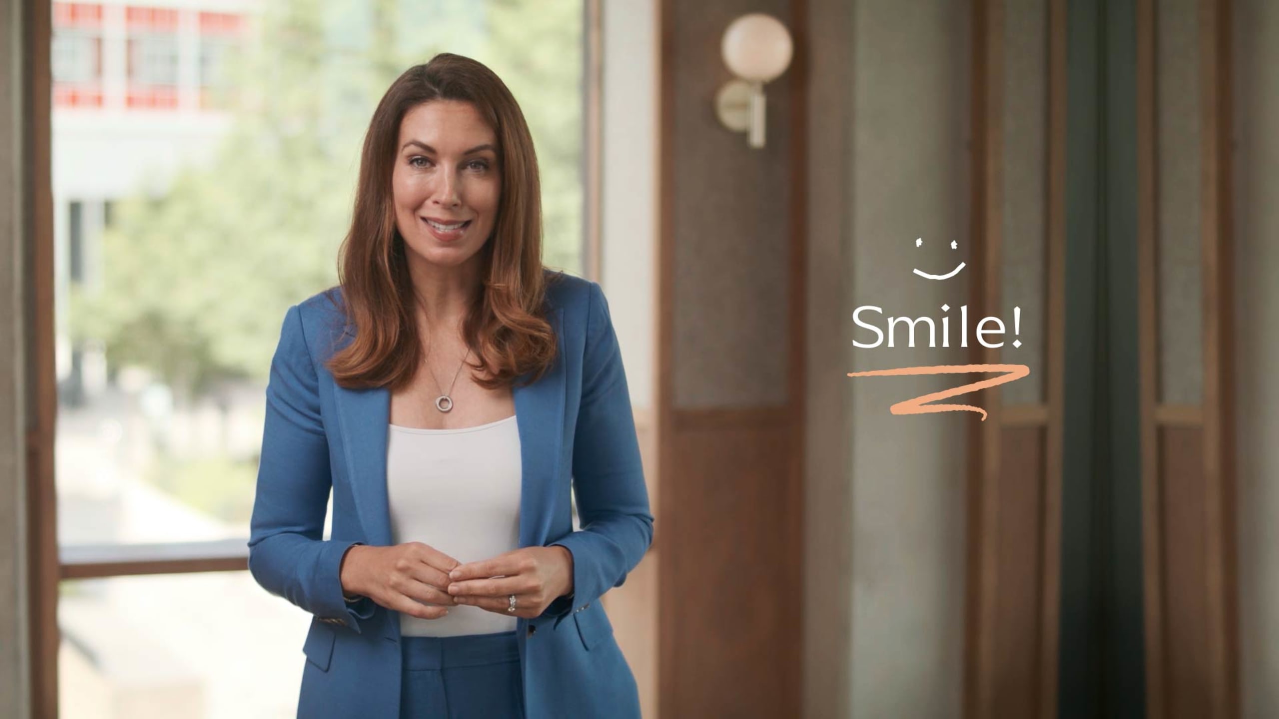 A woman in a blue suit smiles indoors with a "Smile!" text and a smiley face graphic beside her.