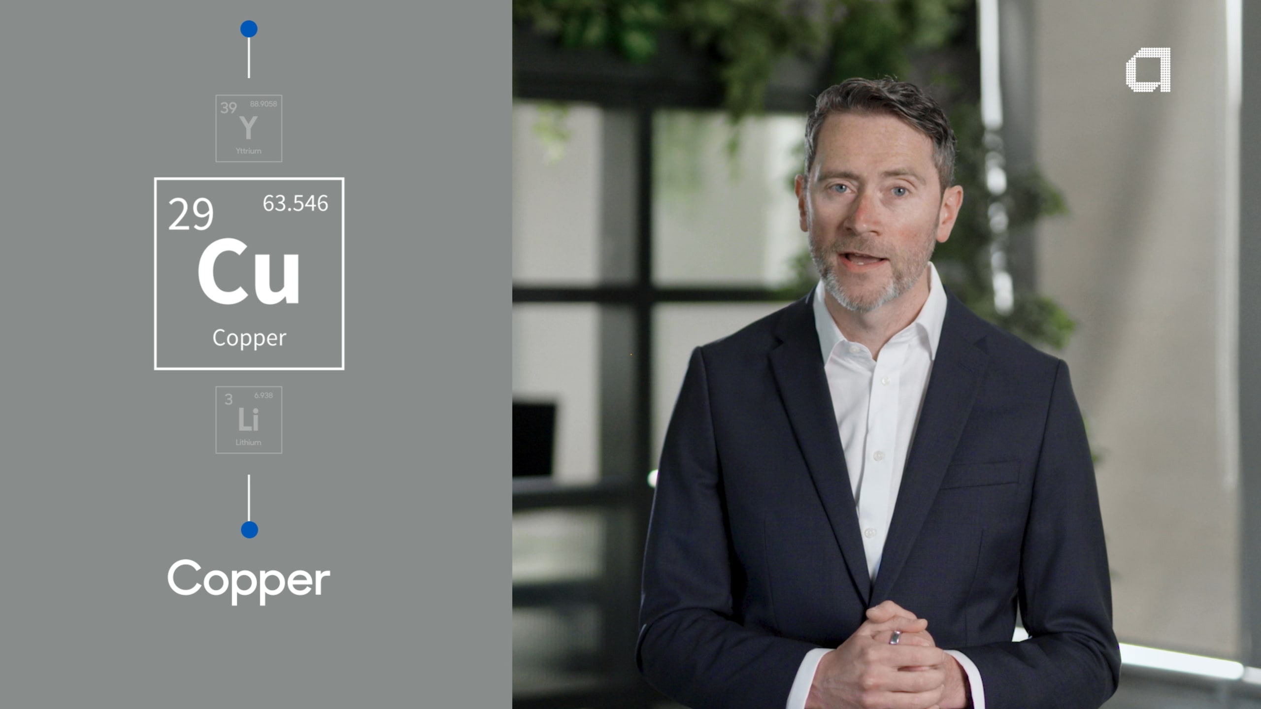 A man in a suit stands in an office setting, with a graphic of the element Copper (Cu) displayed beside him.