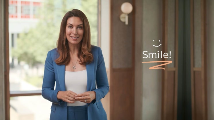 A woman in a blue suit smiles indoors with a "Smile!" text and a smiley face graphic beside her.