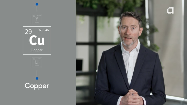 A man in a suit stands in an office setting, with a graphic of the element Copper (Cu) displayed beside him.