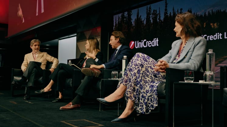 Four people seated on a panel discussion stage, engaged in conversation, with a UniCredit logo in the background.
